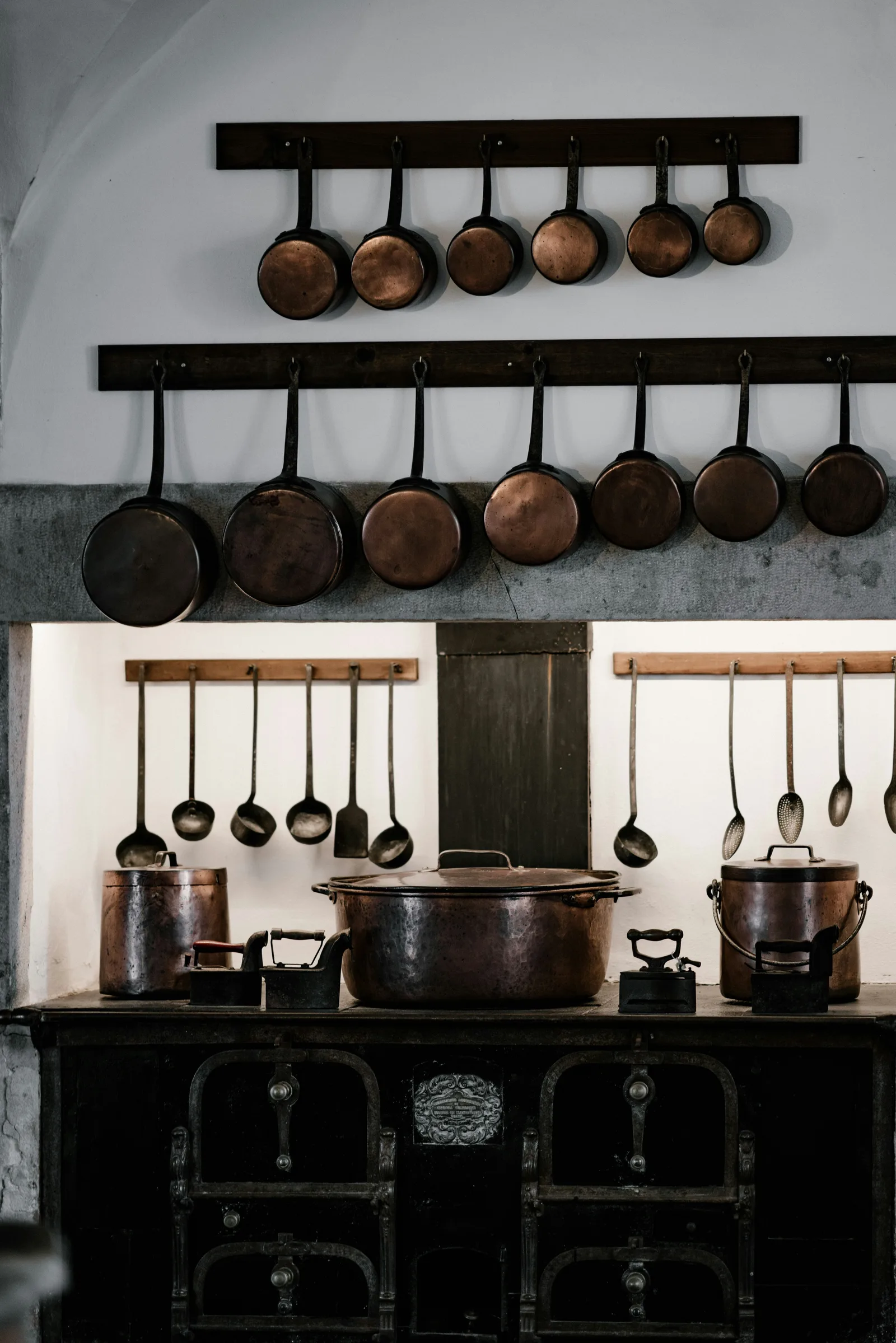 Rows of copper pans and cooking utensils hanging above an antique stove