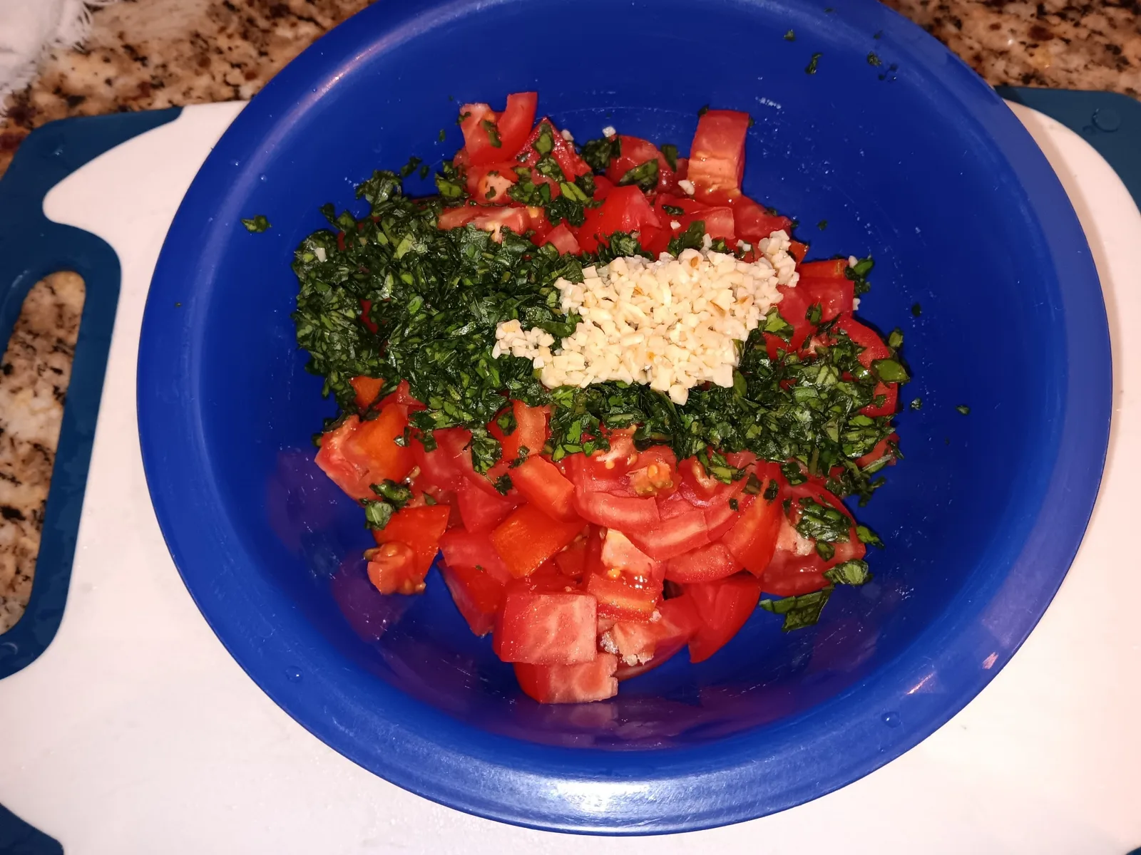 Chopped tomatoes, basil, and minced garlic gathered in a blue mixing bowl