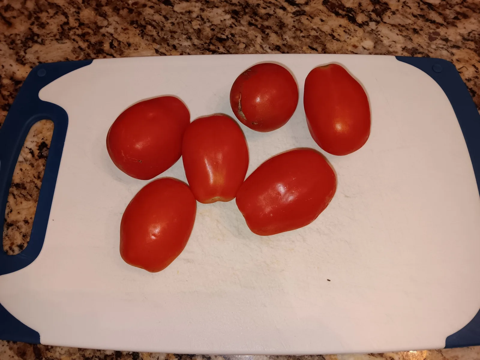 Six ripe Roma tomatoes arranged on a cutting board