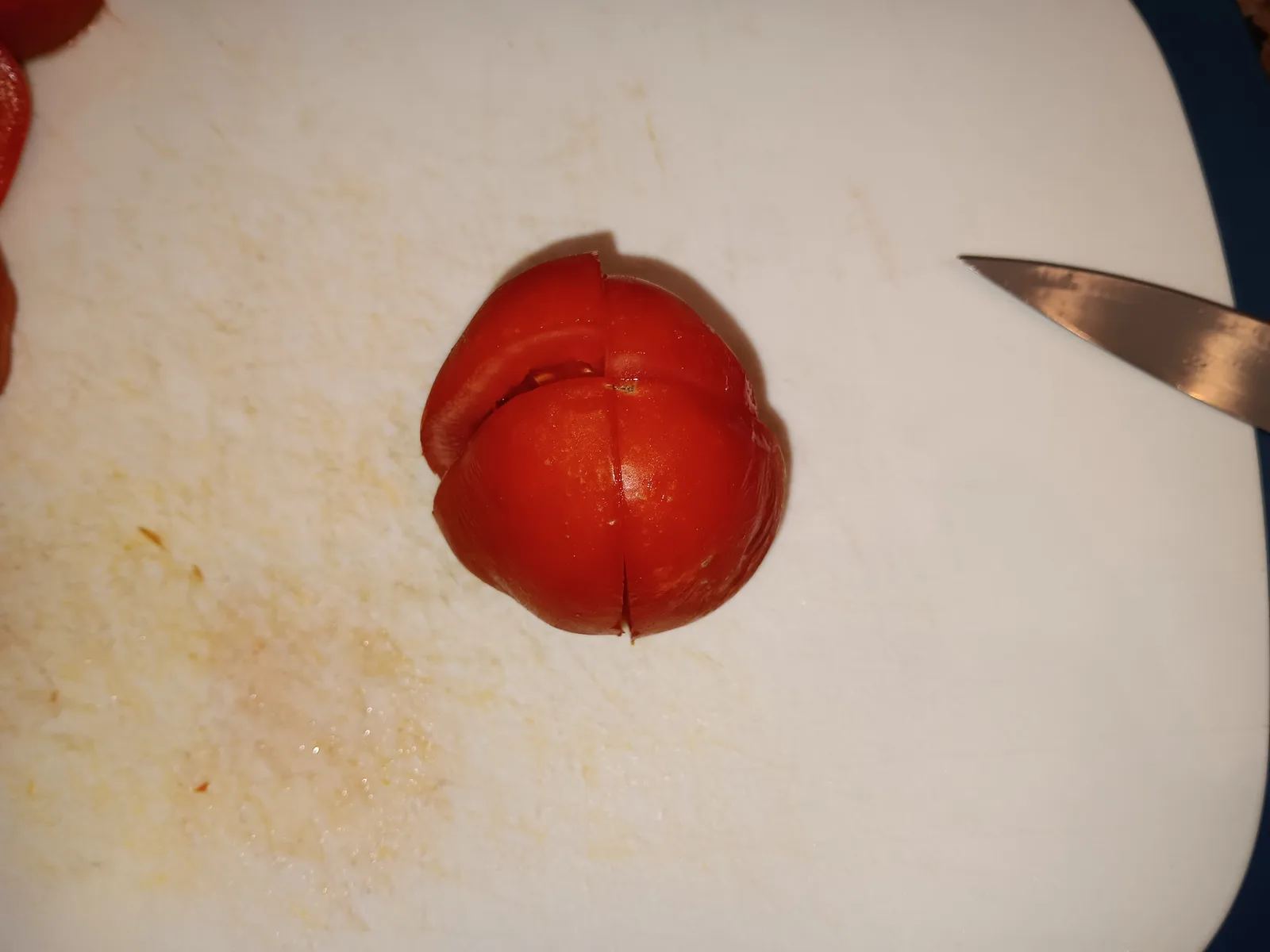 A Roma tomato partly cut into quarters on a cutting board